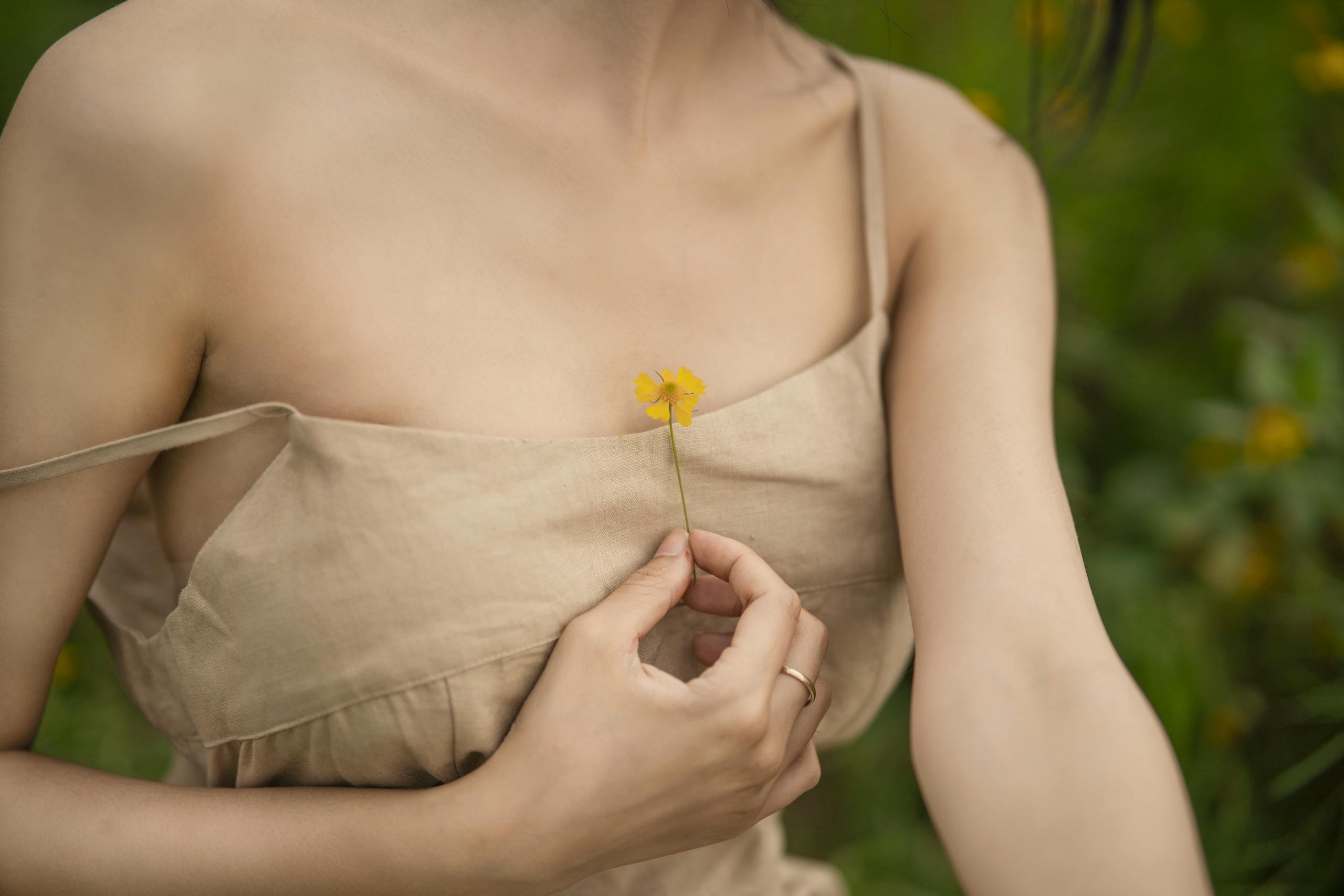 Elegant close-up of a woman in a beige dress holding a yellow flower outdoors. Soft and serene.